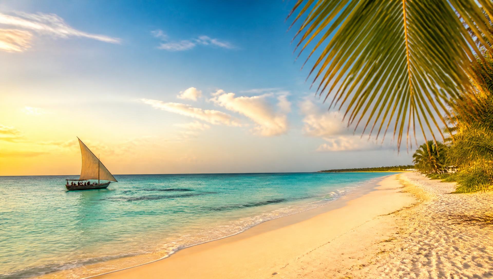 A quiet white sand beach in Zanzibar with a dhow sailing on turquoise water